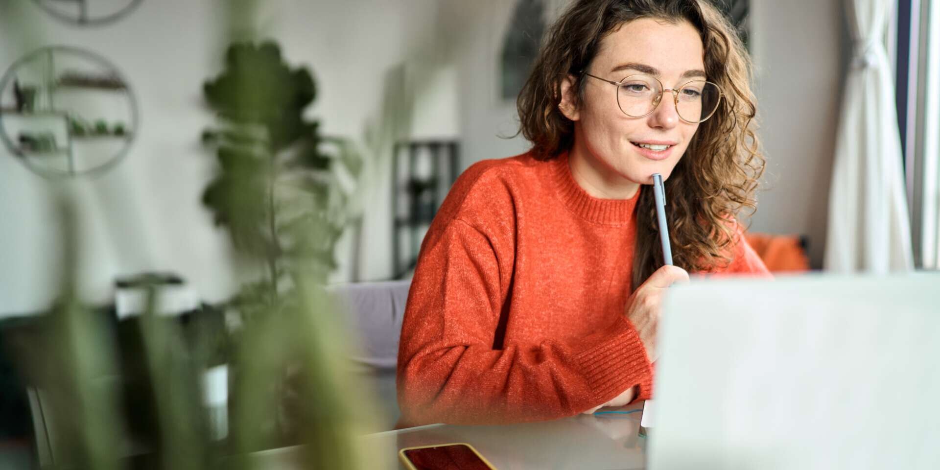 junge Frau sitzt lächelnd vor ihrem Laptop und nimmt an einer Videokonferenz teil