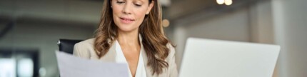 Frau sitzt am Laptop mit Papier in der Hand. Abschlagsrechnung.