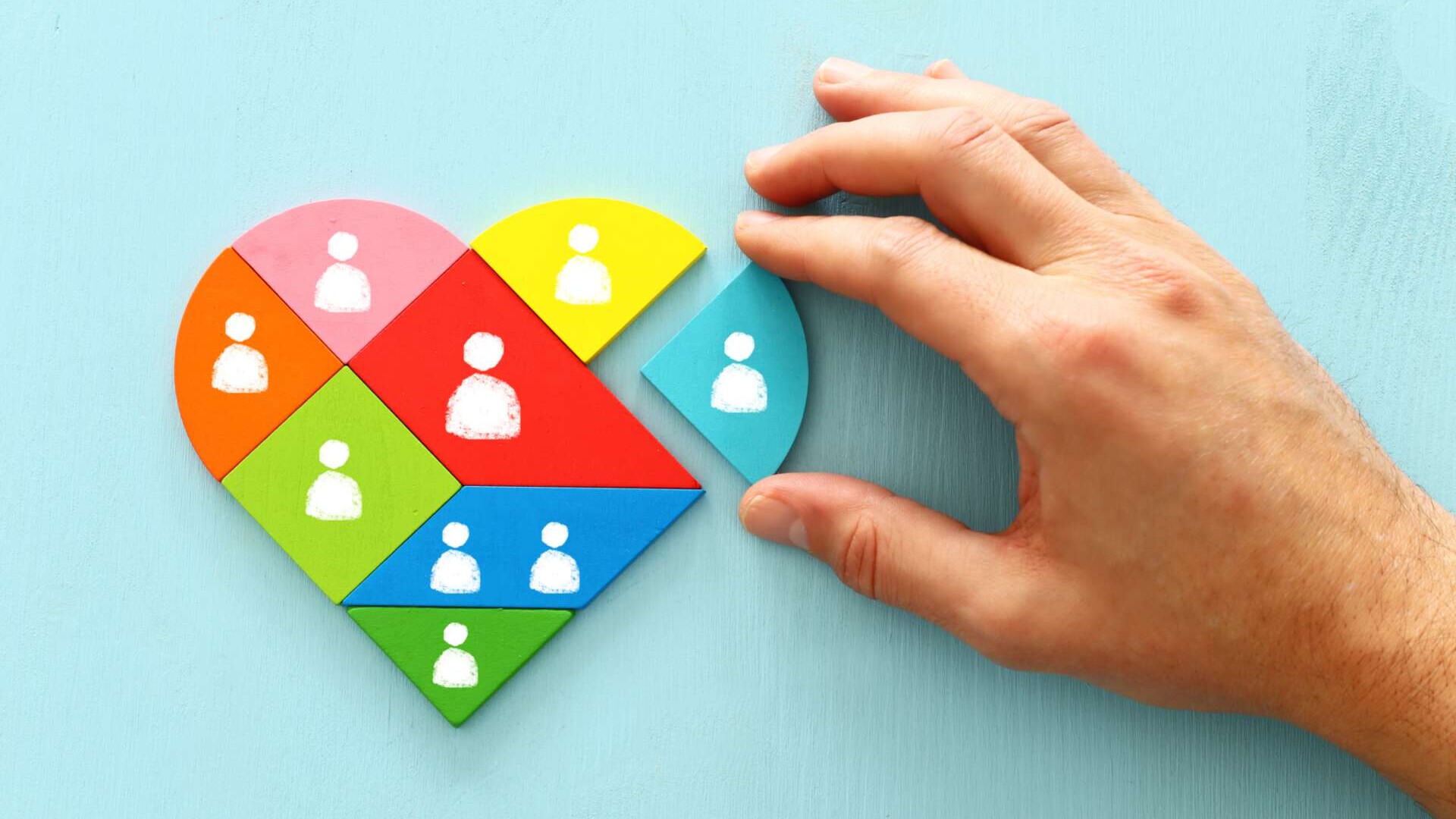 Herz aus Einzelteilen mit abgebildeten Personen , eine Hand puzzelt das Herz zusammen