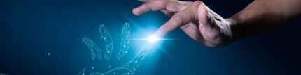 Eine digitale und eine echte Hand berühren sich an den Zeigefingern. Dort leuchtet ein blaues Licht
