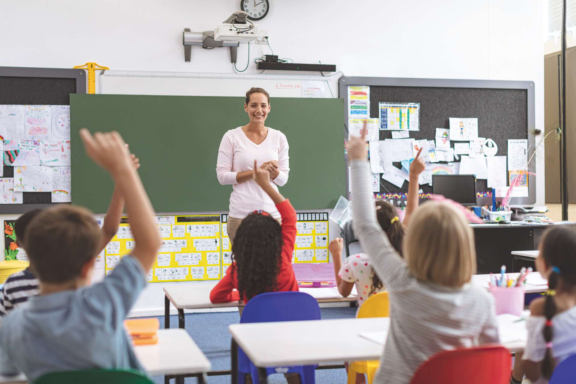 Lehrerin steht in einem Schulklassenzimmer vor Grundschülern an einer Tafel