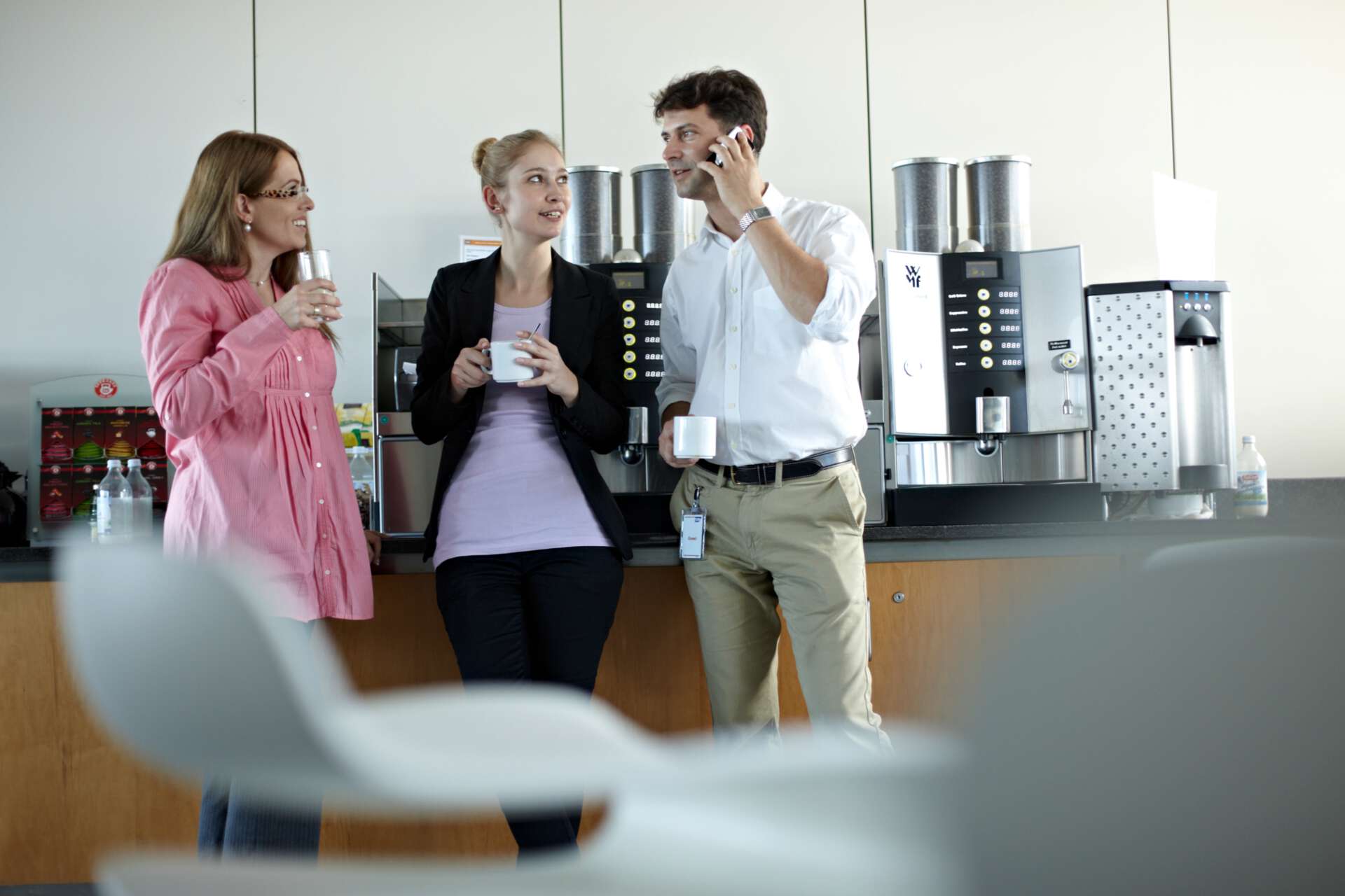 Zwei Frauen und ein Mann unterhalten sich an der Kaffeemaschine im Büro
