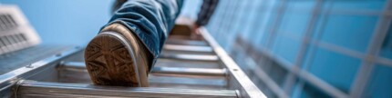 Bauarbeiter, der auf einer Leiter an der Fassade eines modernen Gebäudes hinaufsteigt