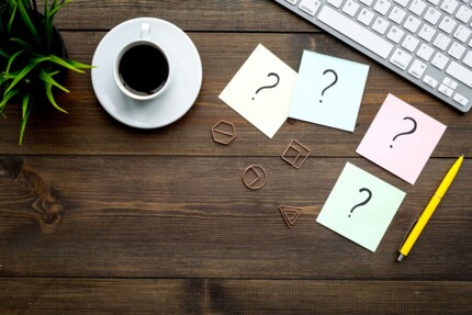 Fragezeichen auf Post-Its auf einem Tisch. FAQ