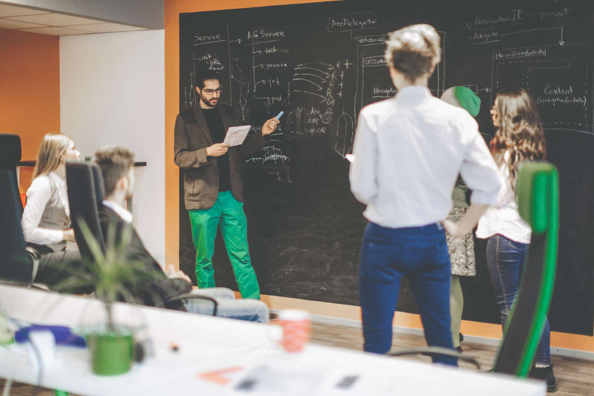 Programmierinnen und Programmierer zeigen an einer Tafel die geplante Software-Architektur an.