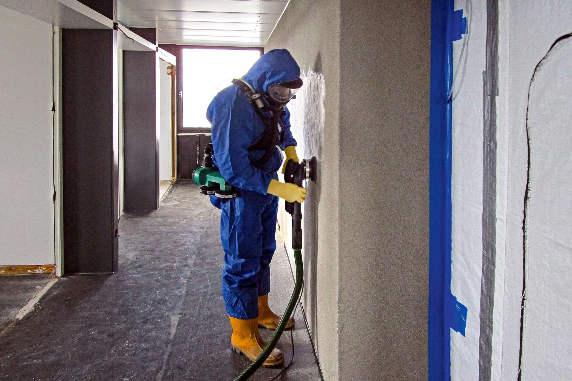 Arbeiter mit persönlicher Schutzausrüstung schleift Wand ab, Baustelle