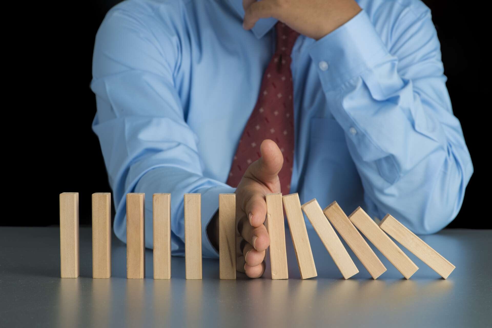 Dominos fallen, Hand eines Mannes stoppt fallenden Dominos und unterbricht die Kettenreaktion.