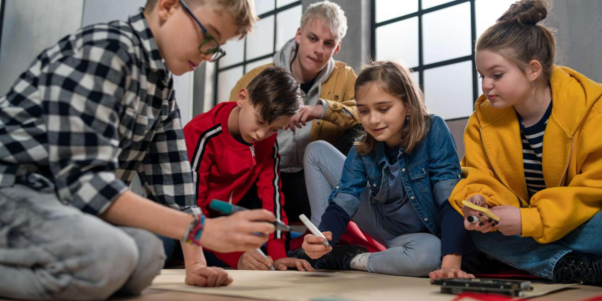 Eine Gruppe Kinder, die gemeinsam mit ihrem Lehrer im Klassenzimmer an einem Projekt arbeiten