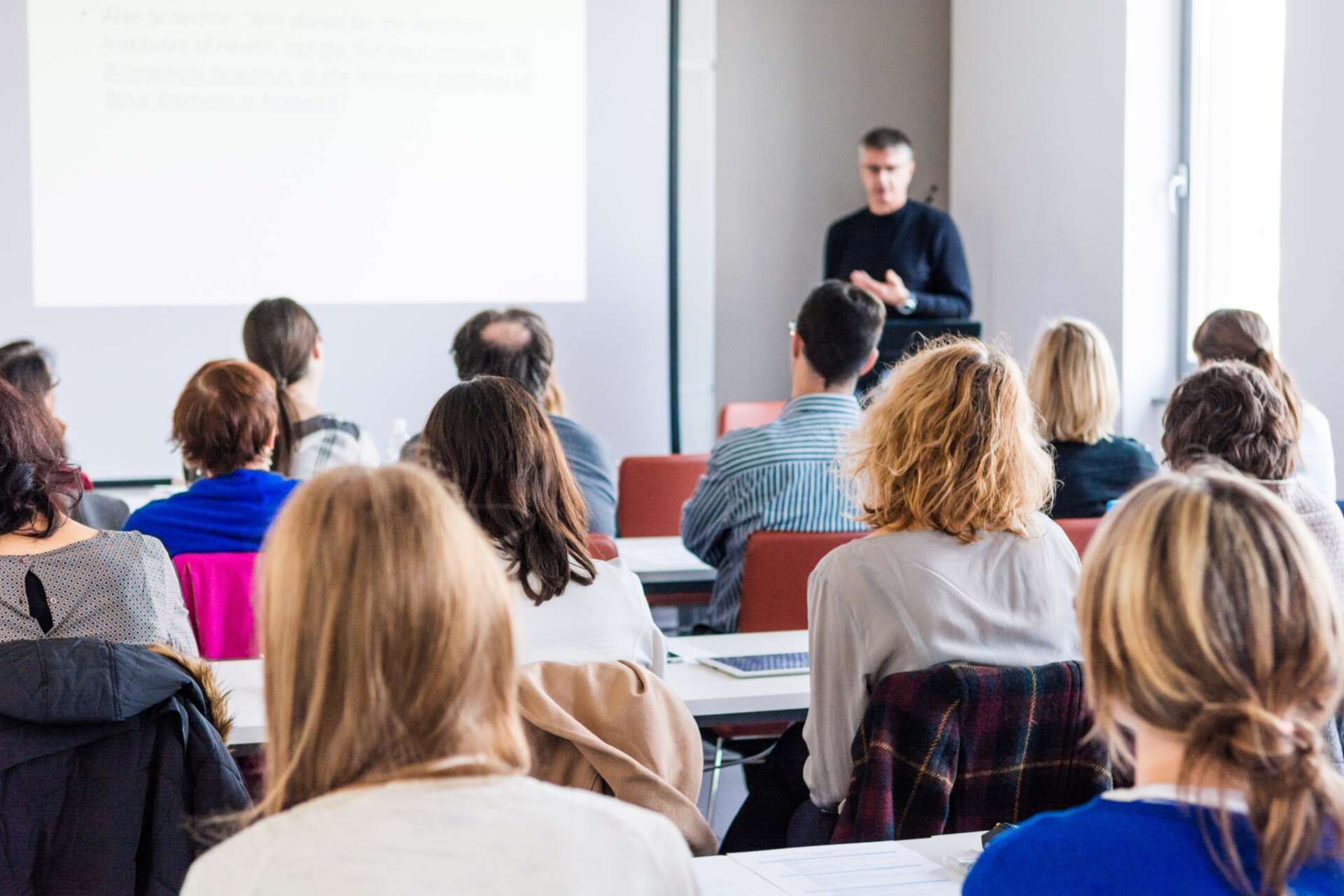 Seminarsituation in Präsenz, Dozent im Hintergrund und Teilnehmende von Hinten