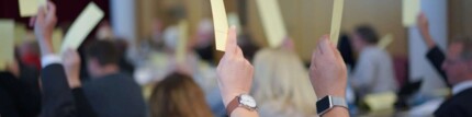 Viele Hände halten einen gelben Wahlzettel in die Luft