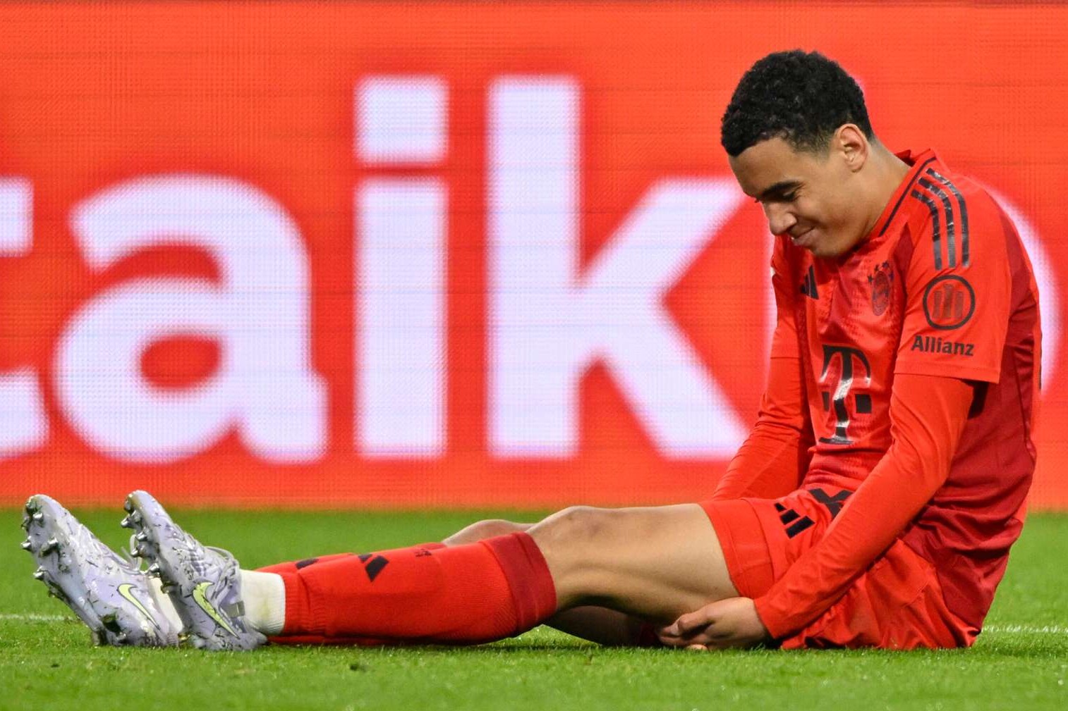 Bayern Münchens Mittelfeldstar Jamal Musiala sitzt während der Bundesligapartie gegen den FC Augsburg verletzt auf dem Spielfeld und hält sich den linken Oberschenkel, 4.04.2025 