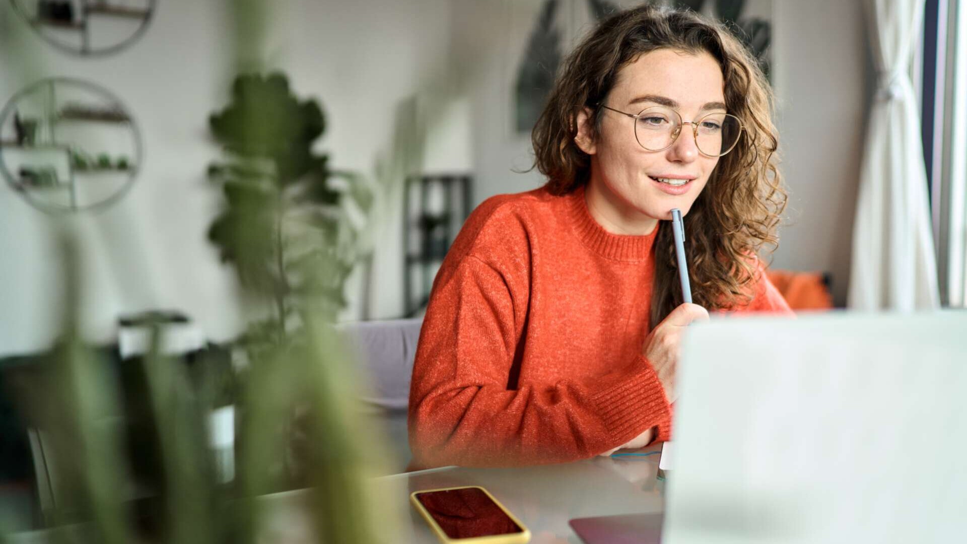 junge Frau sitzt lächelnd vor ihrem Laptop und nimmt an einer Videokonferenz teil