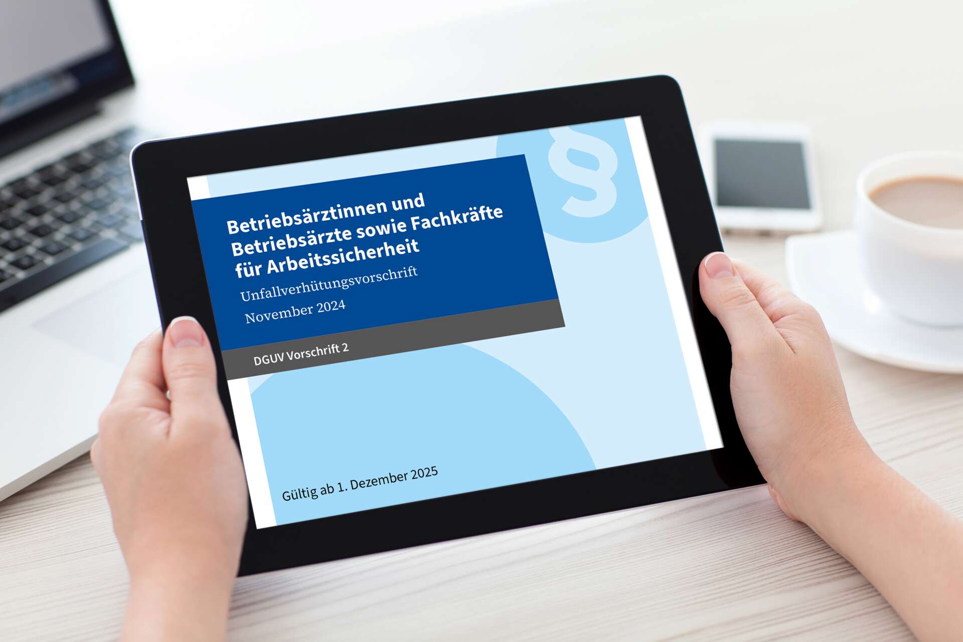 Hände halten Tablet mit Display DGUV Vorschrift 2 vor Arbeitsplatz