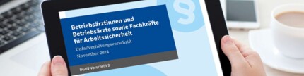 Hände halten Tablet mit Display DGUV Vorschrift 2 vor Arbeitsplatz