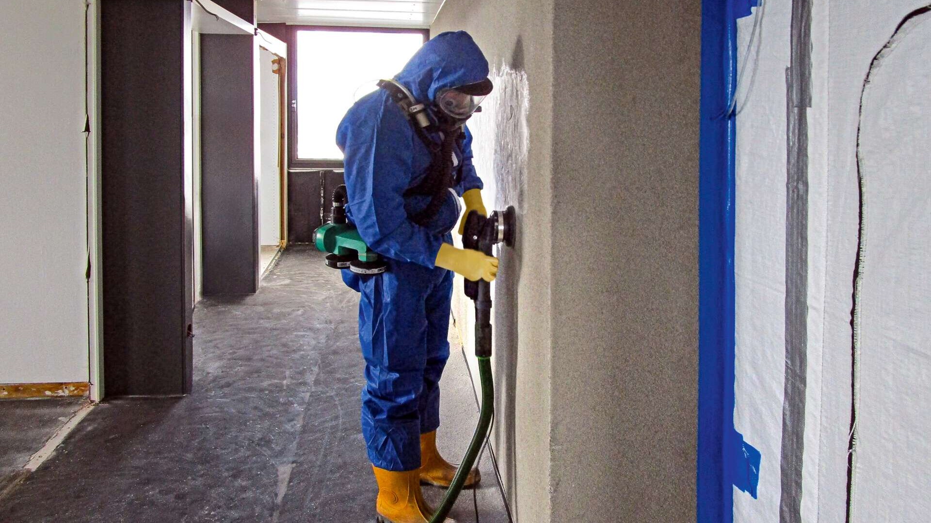 Arbeiter mit persönlicher Schutzausrüstung schleift Wand ab, Baustelle