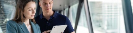 Frau zeigt ihrem Kollegen Seminarbuchung auf Tablet
